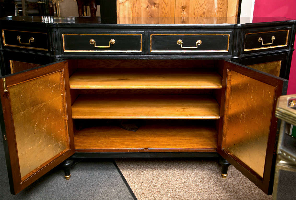 French Louis XVI style ebonized and parcel-gilt sideboard, circa 1950s, the shaped top over a frieze fitted with four drawers, atop a conforming cabinet of four doors with gilt-glass decoration, opens to shelving interior, raised on tapering bulbous