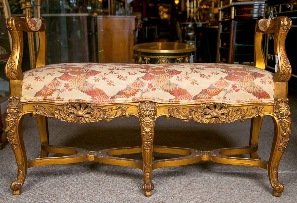 French Louis XV style gilt bench, circa 1930s, overall gilded and distressed, padded arm and seat over a scalloped frieze with cartouche carving, raised on cabriole legs with double X stretcher by Jansen.