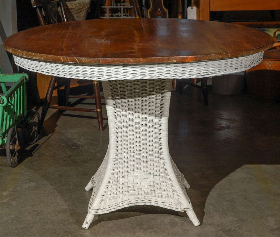 A good size and useful American wicker table from an earlier part of the 20th century, having a squared central column and resting on splayed legs. The top is wood and has a wicker skirting. Jefferson West antiques offer a selection of wicker and