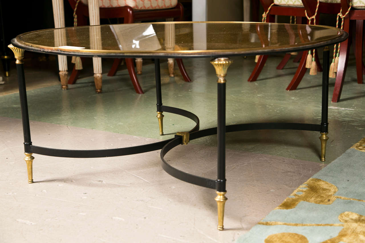 Gold-leaf glass top supported by four metal legs headed by brass accents, two half-moons shaped stretchers joint together, raised on gilt-brass pegged feet.