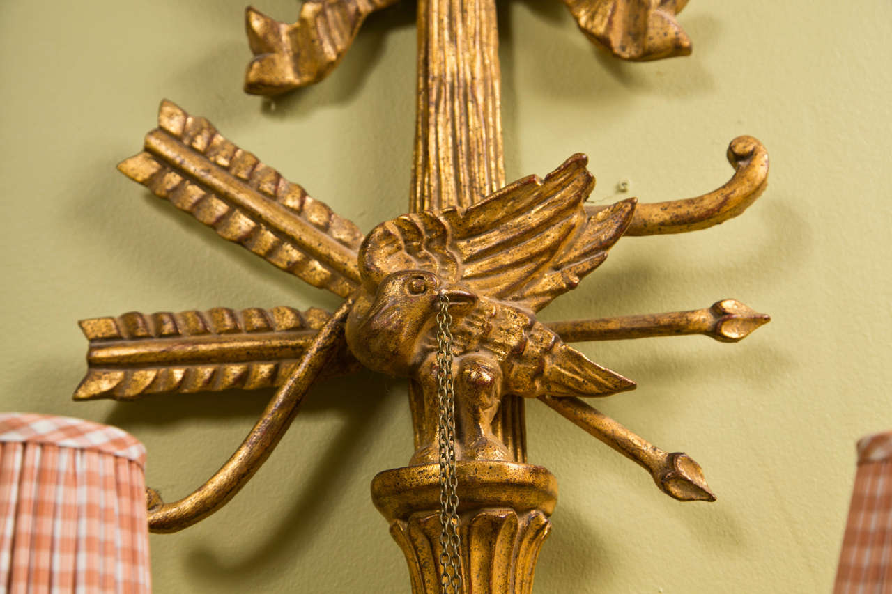 Pair of French two-arm giltwood wall sconces, circa 1940s, each has a ribbon crest extending to arrow and pigeon decoration, each having two arms with fabric shades.
