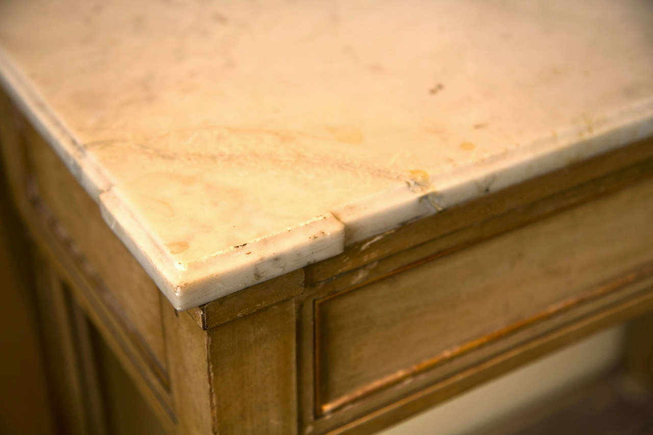 French distress painted and parcel-gilt side table in the Louis XVI style, circa 1940s in original condition. The shaped white marble-top a frieze fitted with a single drawer, supported on four fluted legs joint by a lower tier, raised on toupie