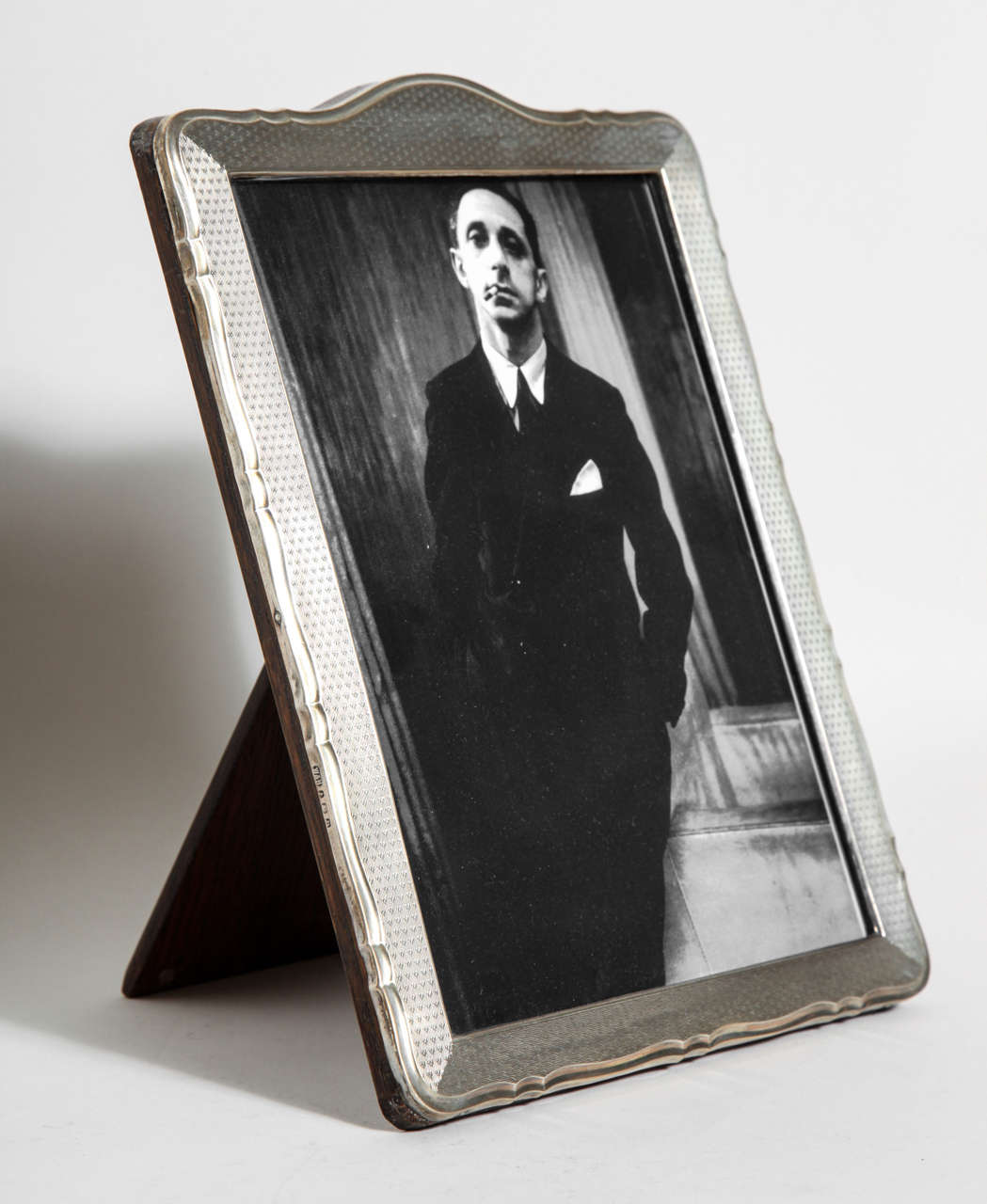 Sterling silver photograph frame with engine-turned decoration on face, arched top and serpentine border and with original oak back and stand.
Hallmarks: 925 silver/ Birmingham/ 1928/ W & H.