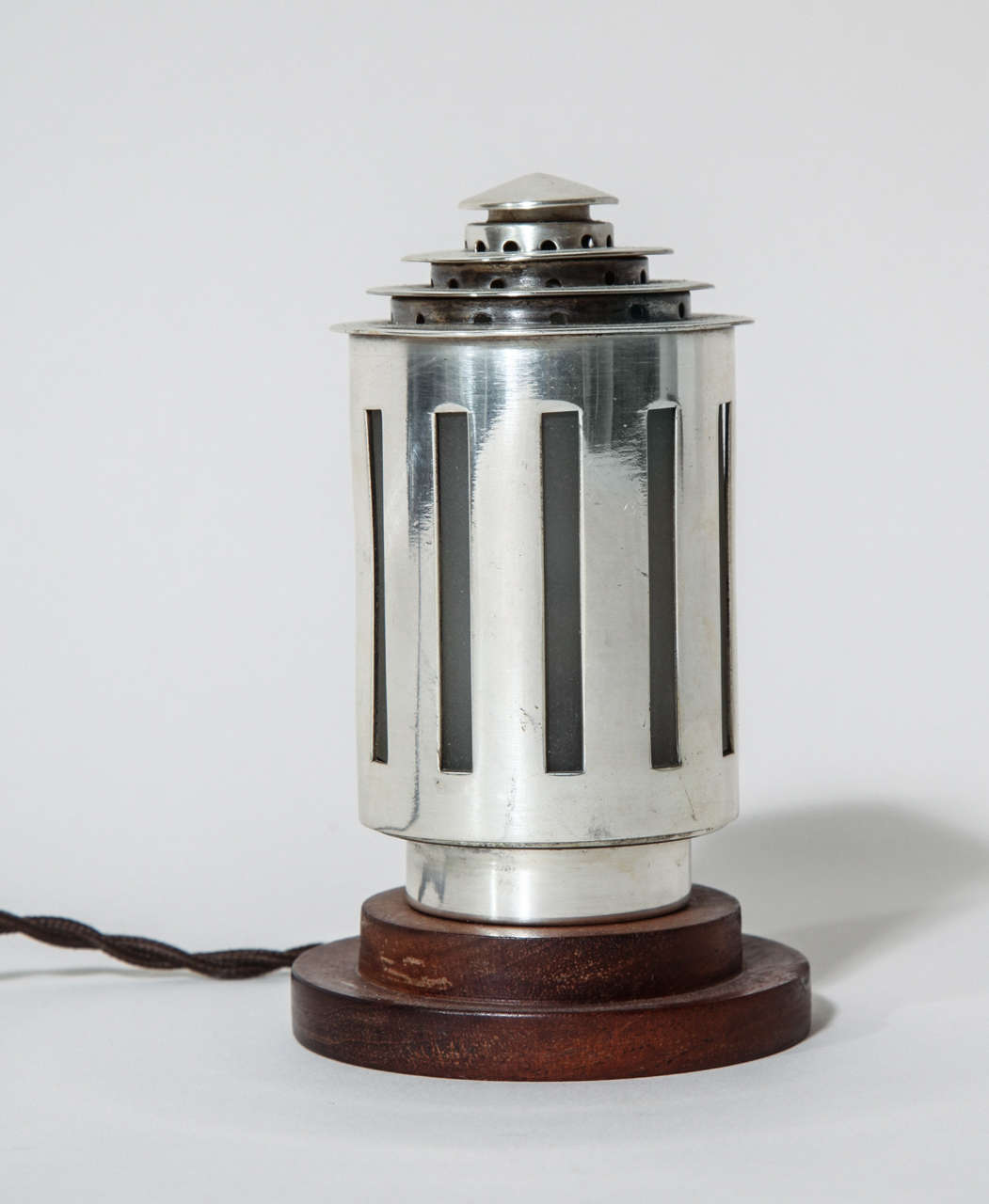 Nickelled metal cylinder with vertical openings over frosted glass cylinder with stepped top on stepped wood base.
Stamped: DESNY PARIS/ MADE IN FRANCE/ DEPOSE

M. Desnet and Clement Nauny (1900-1969), who in 1927 with the financial backing of M.
