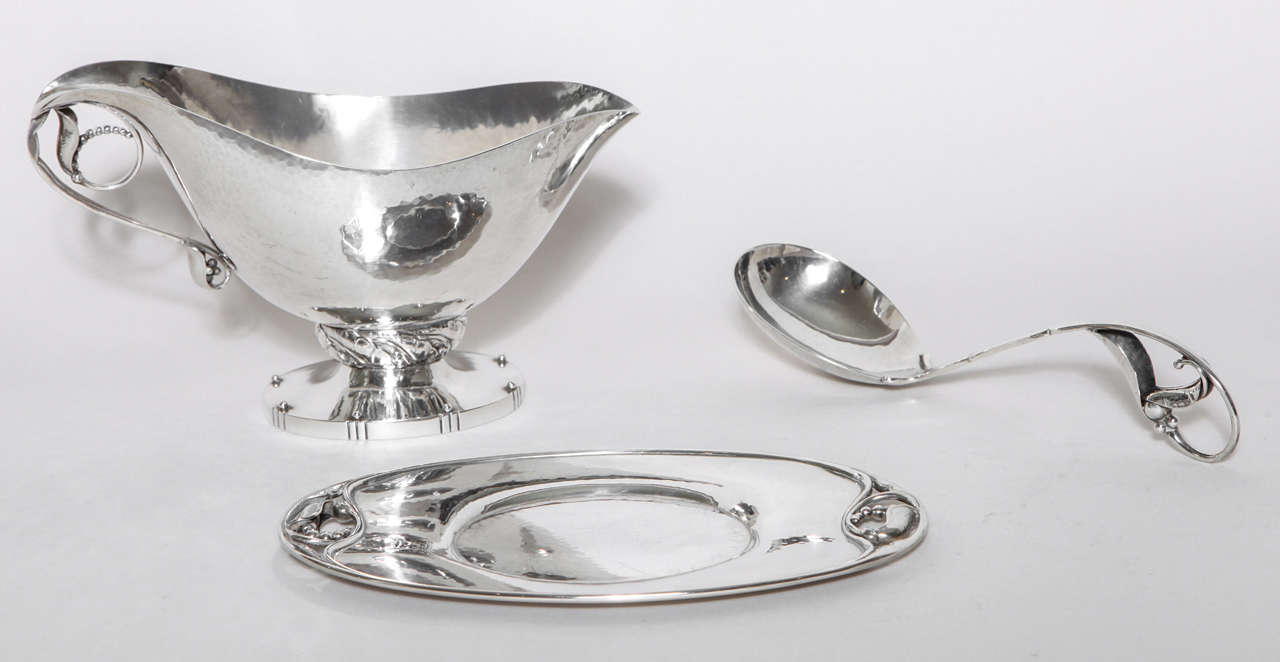 With beaded foliate handle and on pedestal foot, oval stand with openwork foliate bead ends and blossom pattern sauce ladle.
Sauce boat and stand hallmarks: Georg Jensen mark for post-1945/ 177 A/ DENMARK/ STERLING.
Sauce ladle hallmarks: Georg