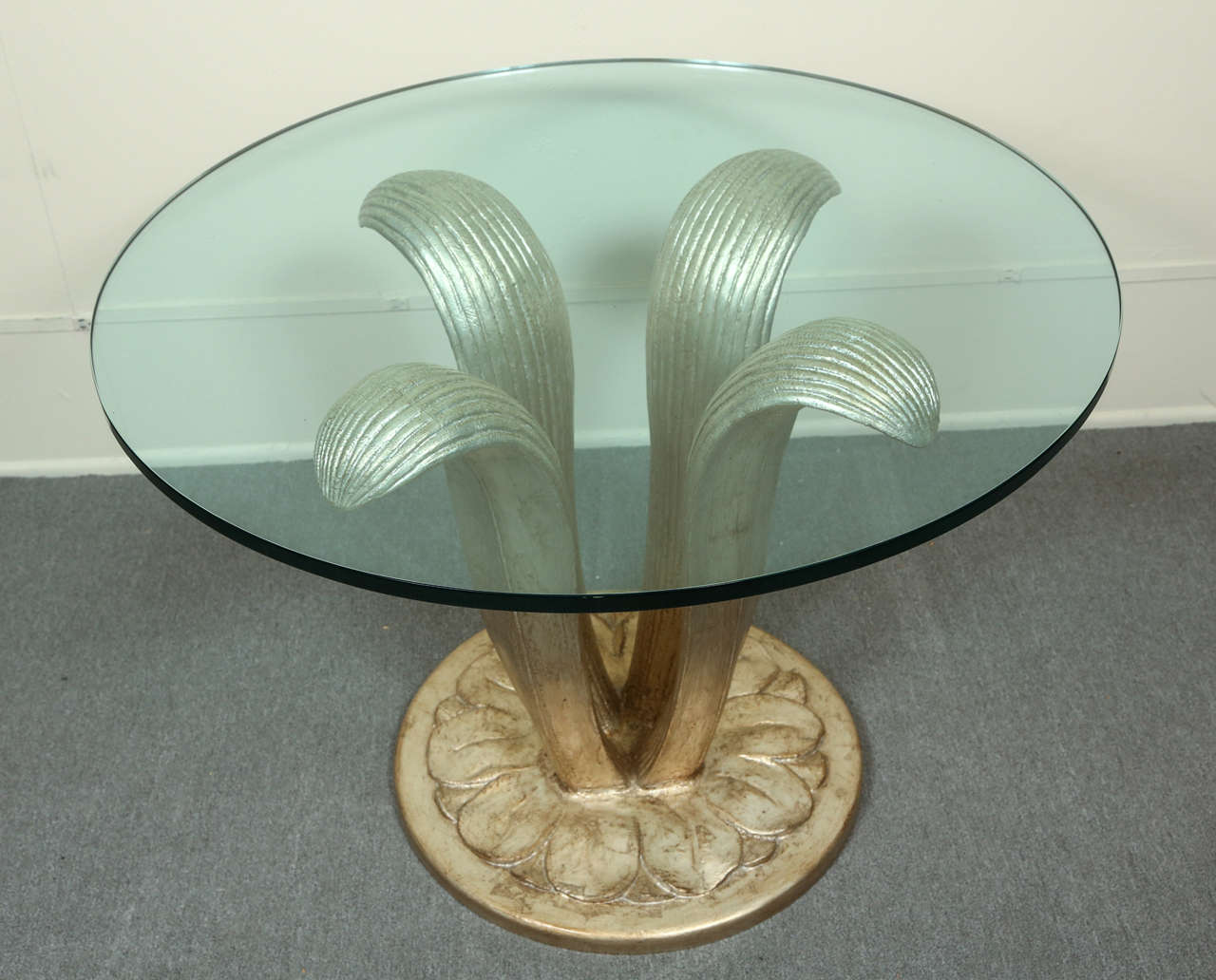 Beautiful large center table with a carved wooden base of graceful leaf forms.
The table is finished in a glazed silver leaf finish which has clear disks that supports a 3/4