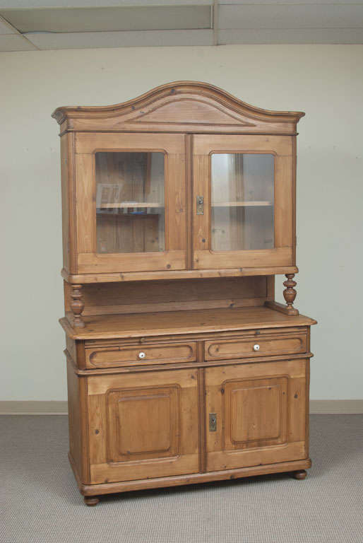 A very handsome Baroque-style glazed dresser featuring a bonnet-topped upper section with two glazed wide-swinging doors above a two door two drawer base with pull-out breadboard and original ceramic knobs.