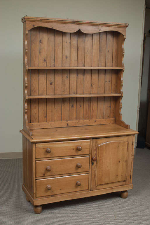 A most attractive cottage open rack dresser featuring three drawers and a single door to the panelled-sided base. The shallow open rack is distinguished by scalloped sides and frieze with two plate-grooved shelves and tongue and groove backboards.