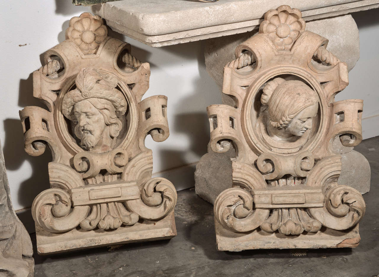 This is a fantastic pair of antique French terra cotta architectural cartouches featuring sculptural portrait heads of a man and a woman in the central oval motif.  Their headdress is of the period and their gaze is downward and slightly towards