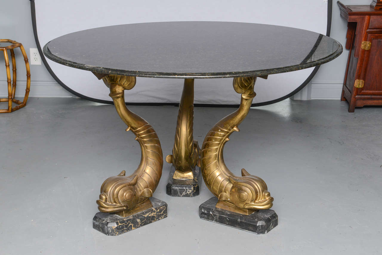 Mid-Century Ubatuba marble-top round table with three solid brass dolphins on marble bases. The brass dolphins have a nice original patina.
Ubatuba marble comes from Brazil and is a finely textured granite featuring black, gold, gray and green