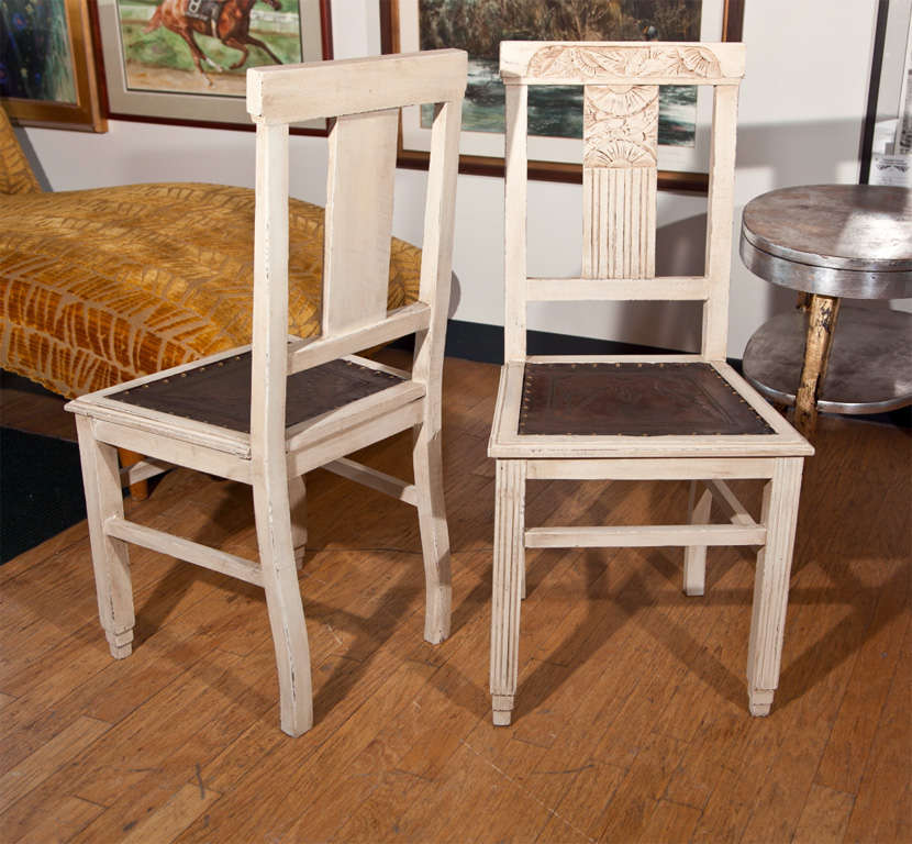 Carved back, birch wood. Seats are hand-tooled brown leather with French natural nail trim. Painted off white finish with glazing highlighting carving.