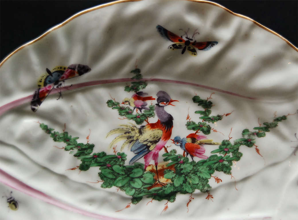 Early production of The Worcester factory in the form of overlapping cabbage leaves. The naturalistic polychrome painting is of an exotic bird perched on a swagged vine with butterflies and a yellow lady bug. The two main veins of the leaves are a