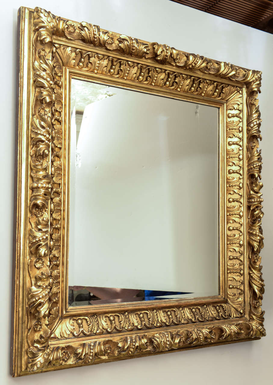Miroir en bois doré, finement sculpté de feuilles d'acanthe, de volutes et de perles, inséré dans un miroir rectangulaire biseauté plus récent.
