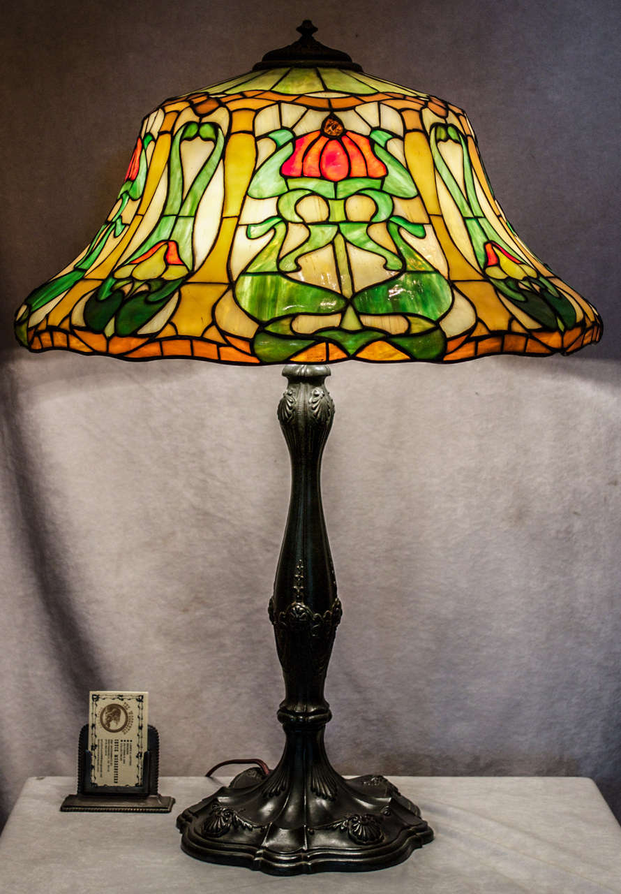 This beautiful leaded glass lamp was done by the Wilkinson Company, Brooklyn, NY, circa 1910.  The shade is done in the art nouveau taste, which is quite unusual.  The base is richly patinated metal and it is an original package.  For a similar