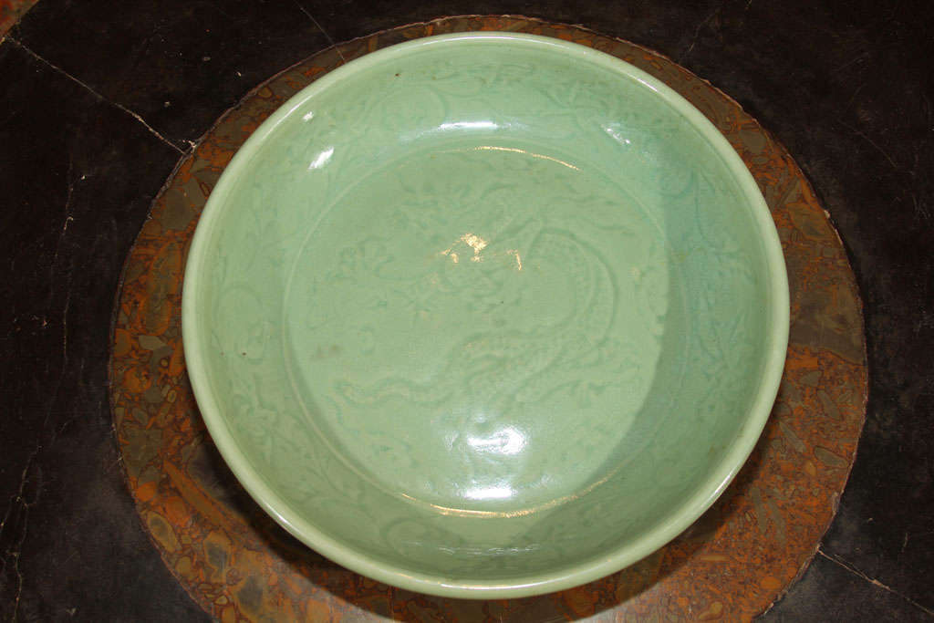 Chinese porcelain charger from the Longquan (Lung-ch’uan) kilns of Chekiang province. Of circular form, with celadon glaze and incised design of a dragon on the inside base and scrolling floral motifs on the cavetto; the exterior without incising