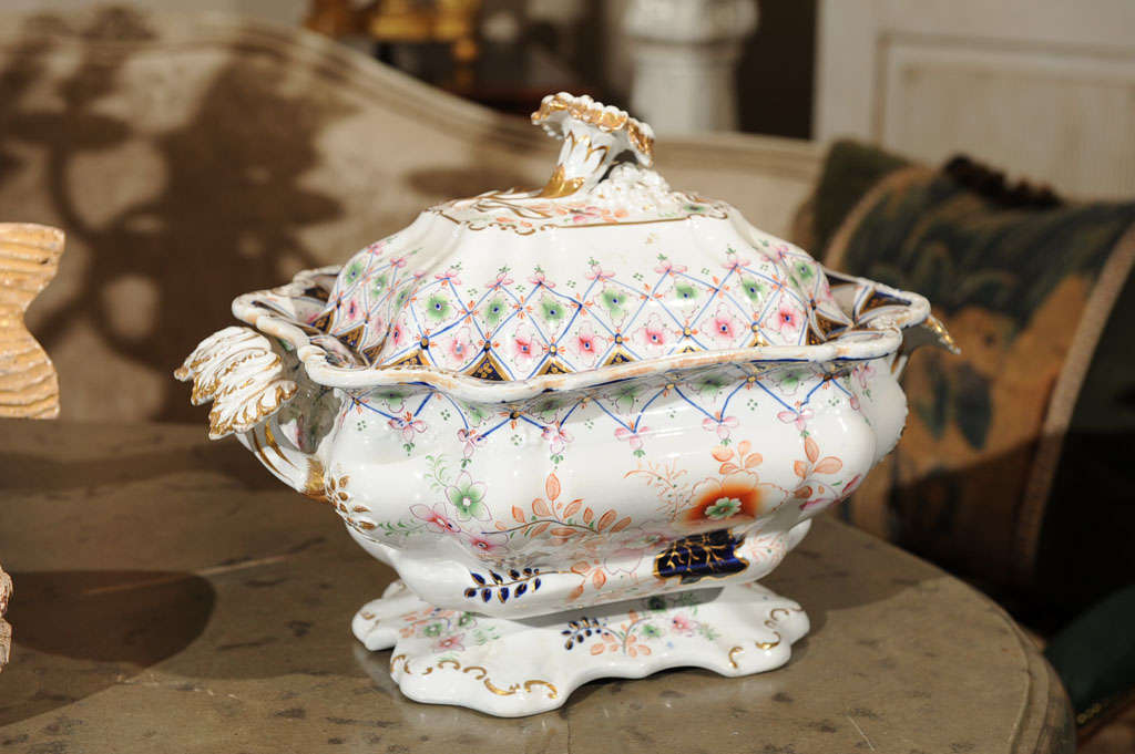 The rectangular bowl raised on a shaped foot flanked by vine handles and fitted with a chrysanthemum final. Overall hand-painted with Imari style foliage in gilt, blue and umber hues. Cover and base marked.