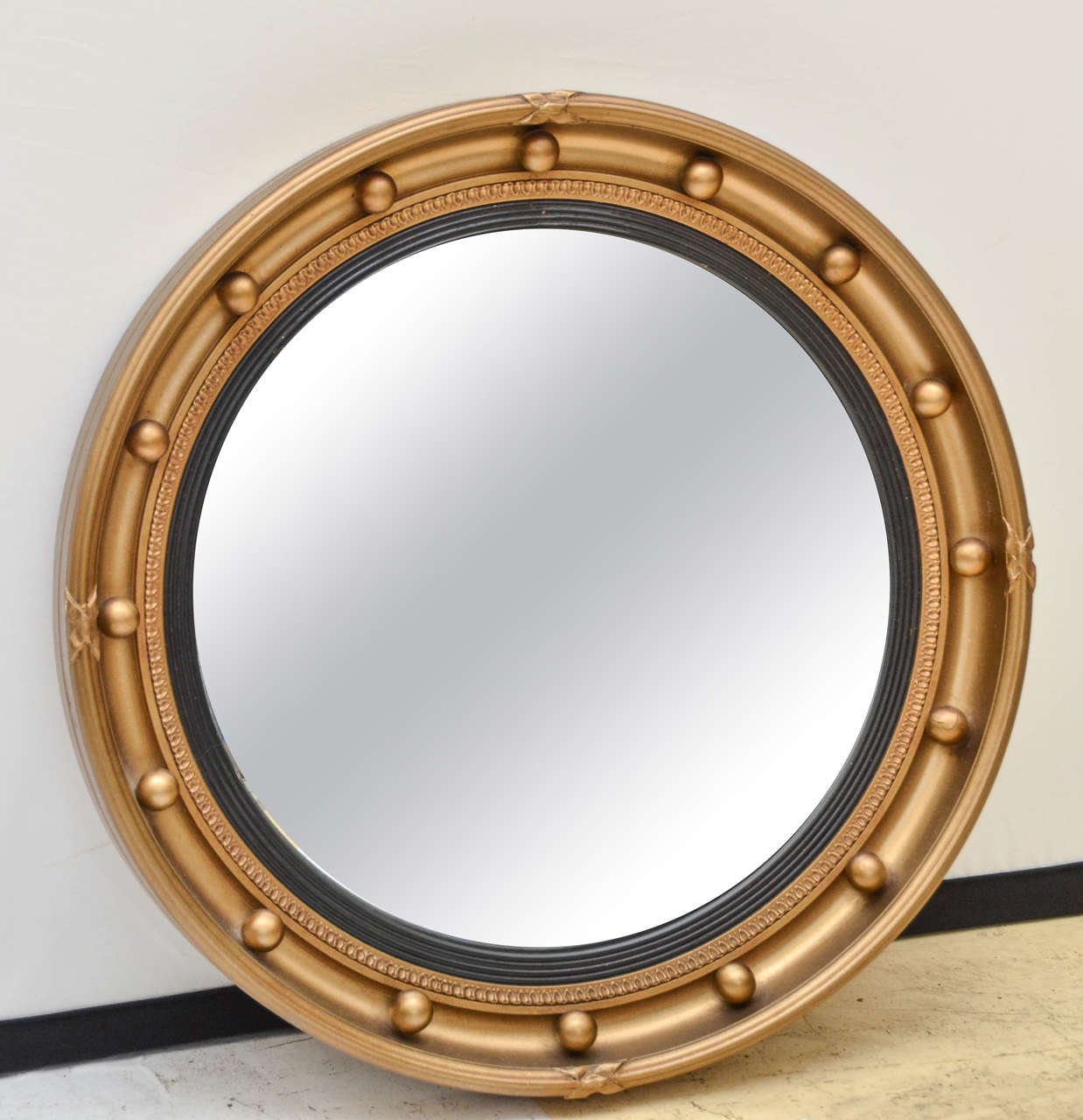 1920s English Regency style bulls eye mirror. The deep molded outer frame has 16 applied balls with a small leaf decorated border. The interior moulding reeded and ebonized. The rest of the frame has a gold toned finish. The back is labeled, Aisonea
