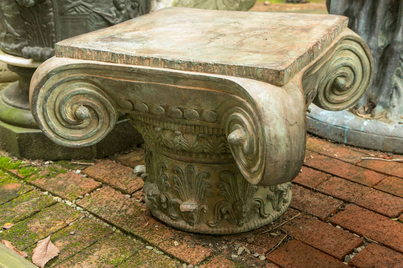 This is a 20th century Corinthian style capital. It has a weathered green patina. The flat surface top measures 18.5 inches square. Well cast, with deep curling corners, and acanthus leaf decoration. It can be used indoors or out.