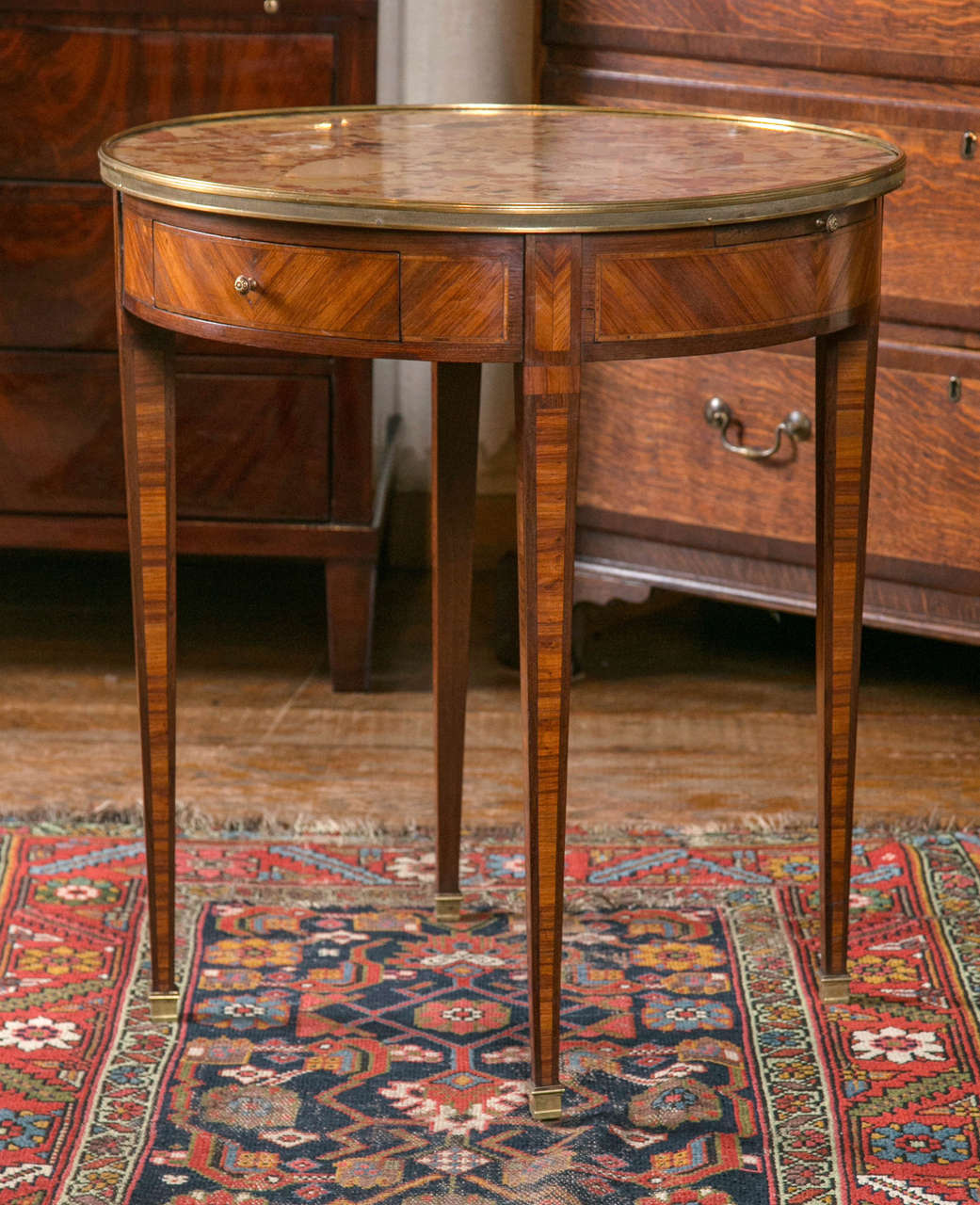 Parquetry in kingwood and tulip wood is expertly employed here to give this table a stately demeanor. The brass gallery surrounding the marble-top does nothing to refute this. Two opposing drawers and candle slides offer extra functions not normally