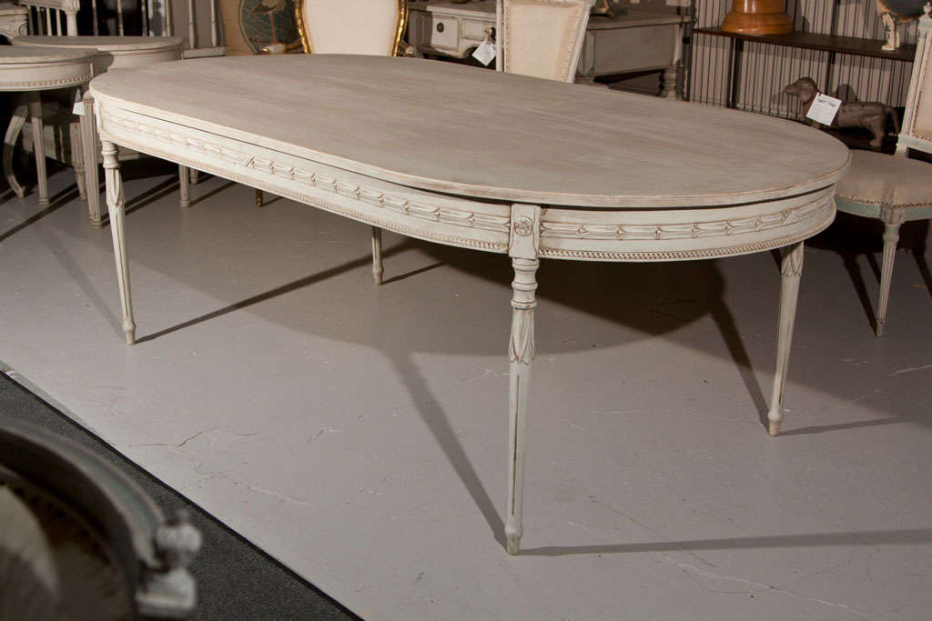 A distress-painted Swedish oval dining table, early 1900s, the oval top over a frieze with elegant carvings of beading, patera, and foliate, raised on fluted tapering legs. No additional leaf.