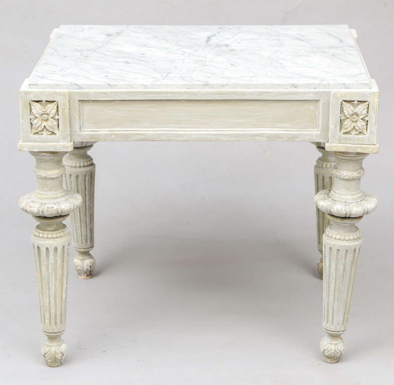 Accent table, having white veined marble top inset in frame of distressed painted wood, with outcarved rosettes at each corner of the apron, raised on round turned fluted legs, terminating in acanthus carved toupie feet.