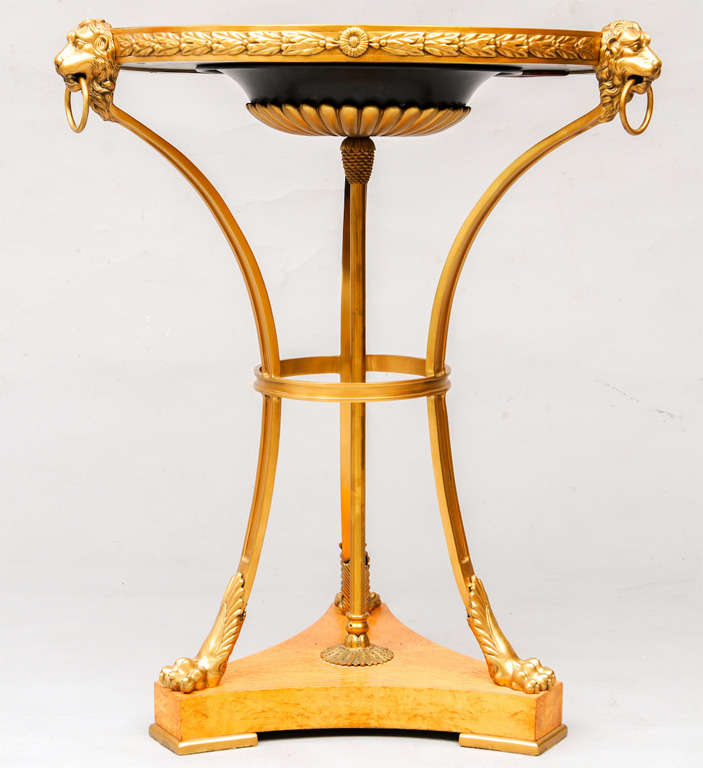 Guéridon, avec un plateau rond en verre bleu biseauté inséré dans un cadre en laiton doré ; son tablier est décoré de détails de lauriers et de rosettes, sur des pieds insérés à chapiteau de masque de lion se terminant par des pieds en patte, reliés