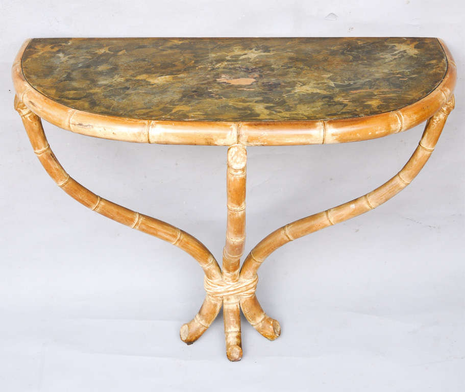 Unusual wall mounting demilune console table, having a faux painted top, on faux bamboo base, three splayed legs joined by carved 