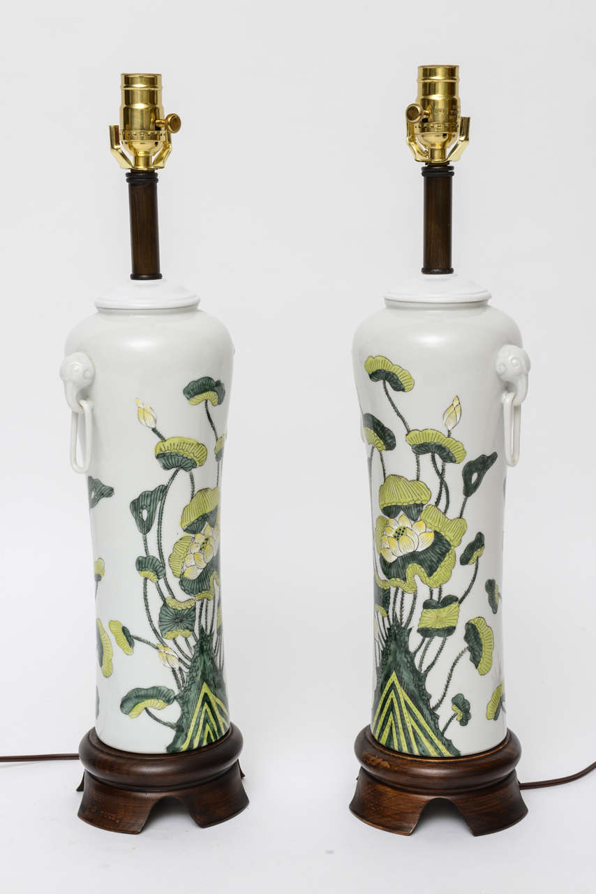 Beautiful 1060s Japanese porcelain vases with lotus flower grouping painted underglaze mounted as table lamps on shaped wood bases. With porcelain rings from the stylised ear handles. Quite beautiful. Rewired and with new brass UL three way