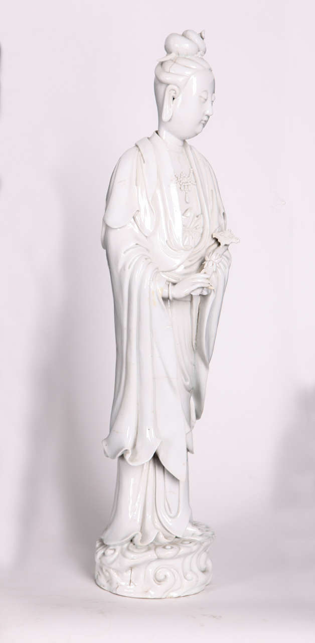 A Blanc-de Chine Figure of Guanyin  Qing Dinasty 
standing on a the waves, the arms lifted to the waist, dressed in loose fitting robes opening at the chest to reveal a necklace, applied with an ivory glaze.
cm 53.