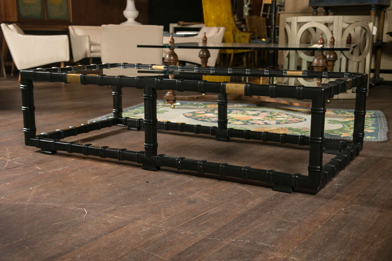 Handsome black painted faux bamboo wood coffee table with three wide brass straps and a glass top.