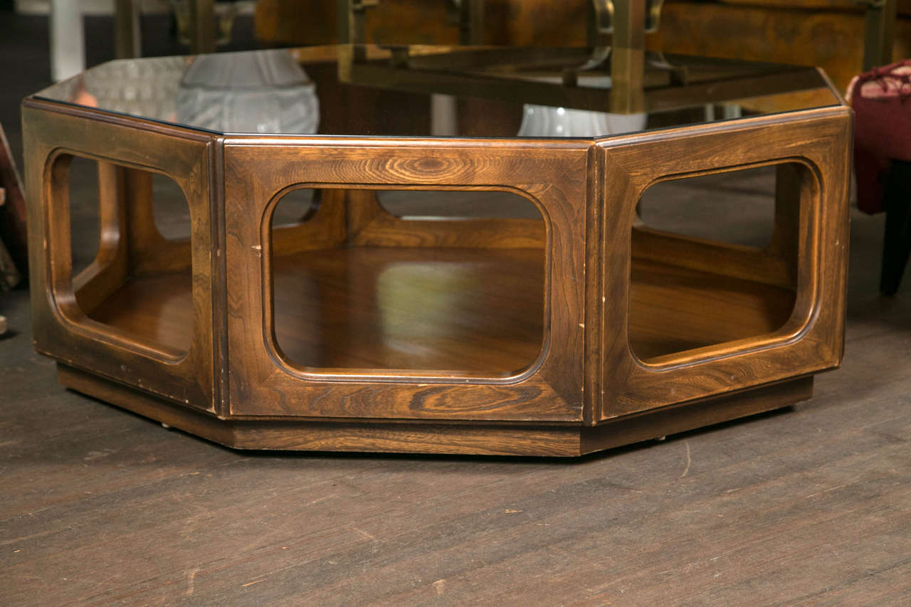 Octagonal dark wood midcentury coffee table on casters with inset tinted glass top.