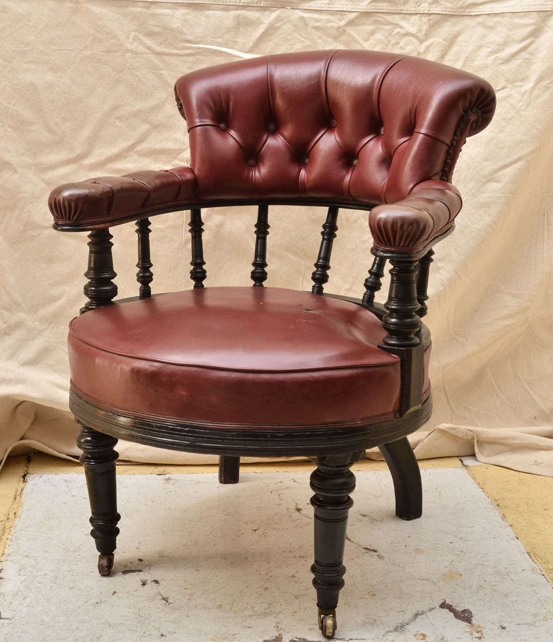 English Ebonised Circular Seat Open Arm Chair . Tufted Out Scrolled Back Rest & Arm Rests Supported By Turned Spindles. Turned Fronts Legs On Castors. Covered In Red Faux Leather. Great Desk Or Library Chair.