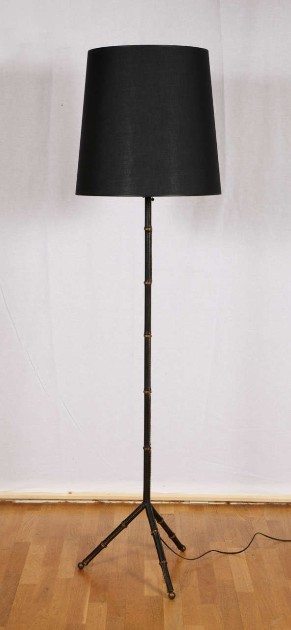 Beautiful bamboo design tripod floor lamp by Adnet circa 1950. Black saddle stiched leather trimmed. Each feet ending with a round brass hoof. The black shade with its gilded interior is new. Good condition. Normal wear consistent with age and