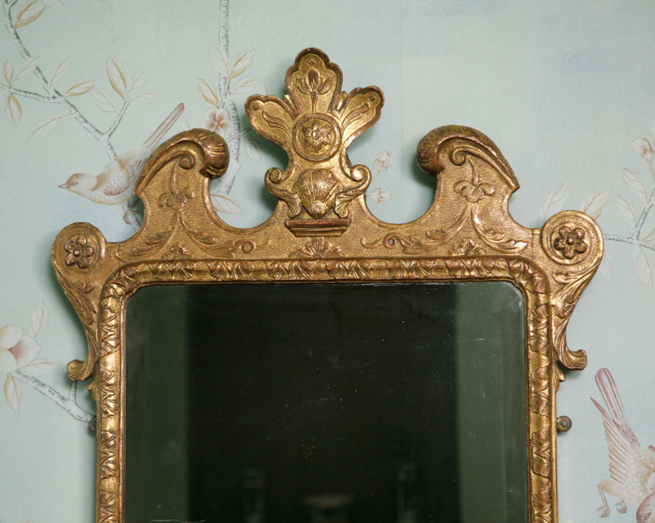 An charming early Georgian carved giltwood and gesso mirror with its original bevelled mirror plate set within a carved and moulded border. Further decorated with flower heads and scrolling foliate decoration on a punched ground centred by a