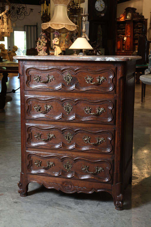 This antique French Louis XV style four drawer chest of drawers has been made from European Oak.  There is an original marble top over a conforming case resting upon 2 scrolled front feet and 2 back block feet.  Each drawer has shaped panel moldings