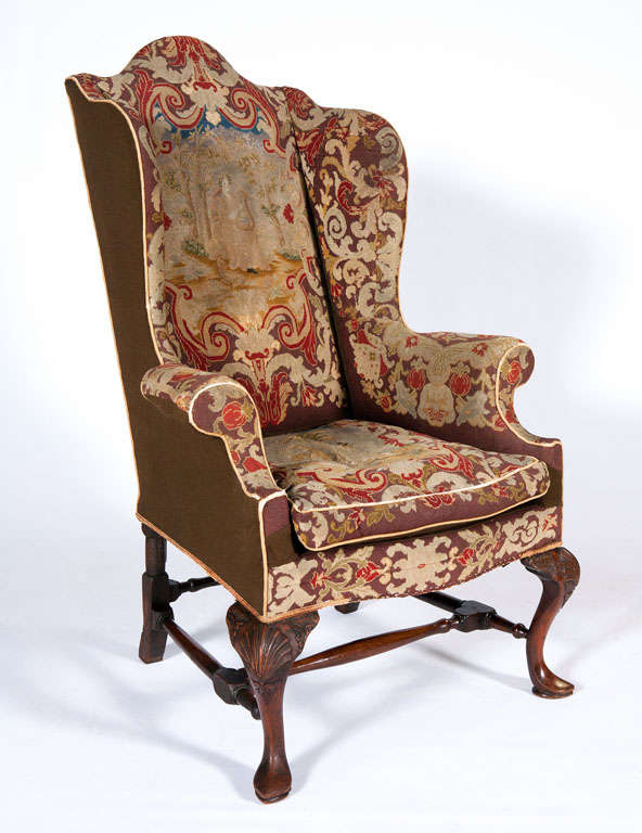 A superb 18th century Queen Anne walnut wing chair. Original tapestry coverings adorn this chair with a lady in a garden with harp scene. The step back arms lead to a scroll arm. The back is arched and top of the chair shaped. The chair is resting