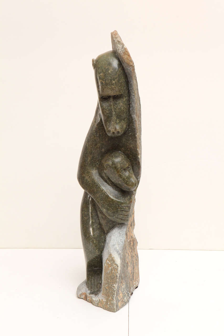 Stone sculpture of a female baboon holding offspring. Back side of sculpture has Stone in rough cut form.