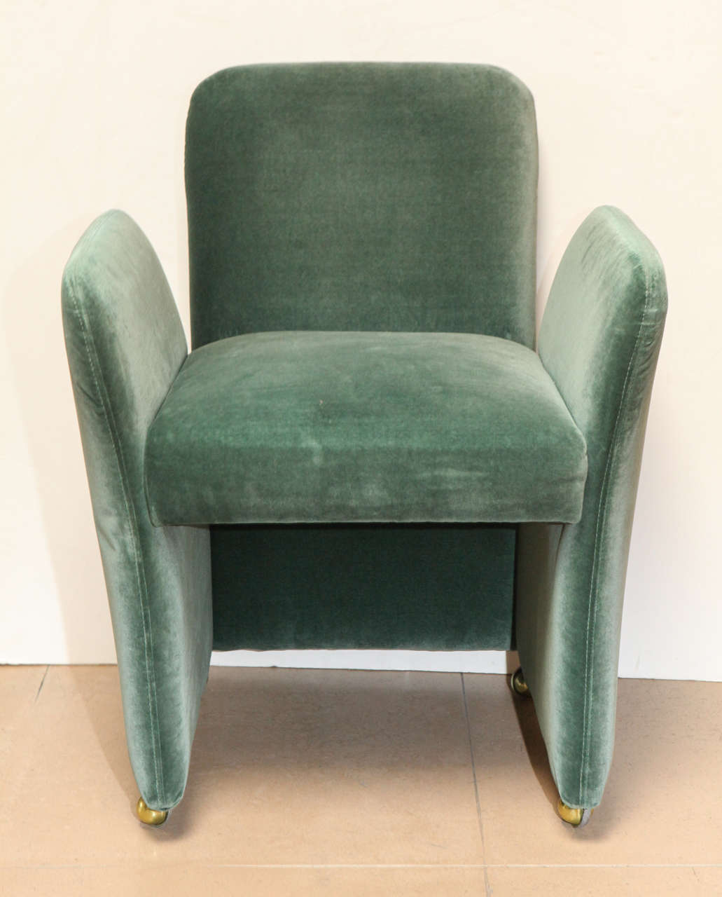 Set of six upholstered pace chairs with emerald green velvet fabric on four brass caster wheels.