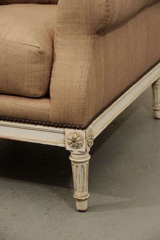 This pair of French Louis XVI style bergeres by Maison Jansen each has white painted fluted legs, topped by rosettes, joined by a molded apron, all supporting an upholstered frame with loose seat and back cushions.<br />
The firm of Jansen was