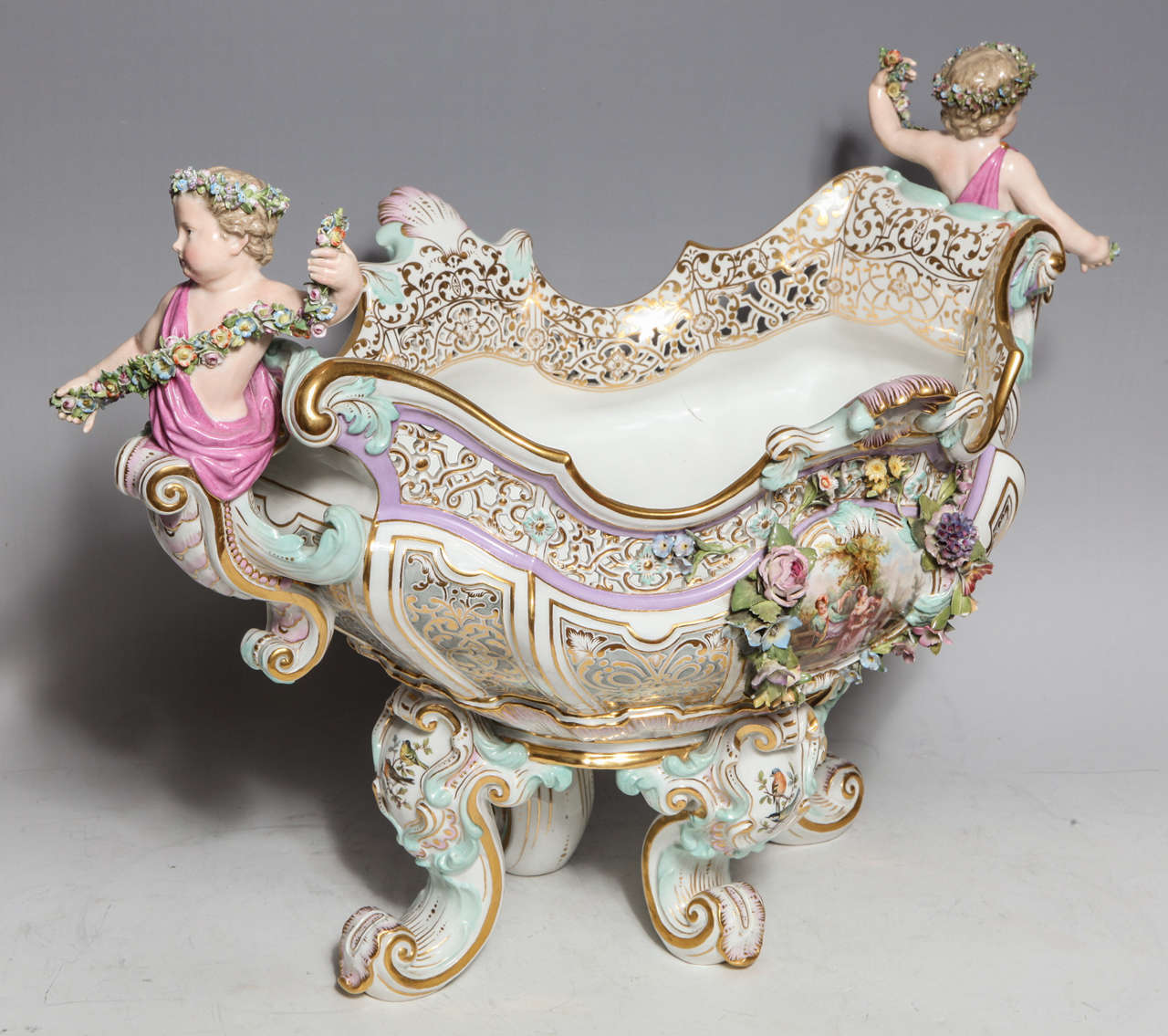 A palatial antique German Meissen porcelain figural centerpiece of exquisite detail embellished with reticulated border, raised flowers, hand painted lover scenes & further adorned with two figures of puttis with garlands of flowers,signed with the