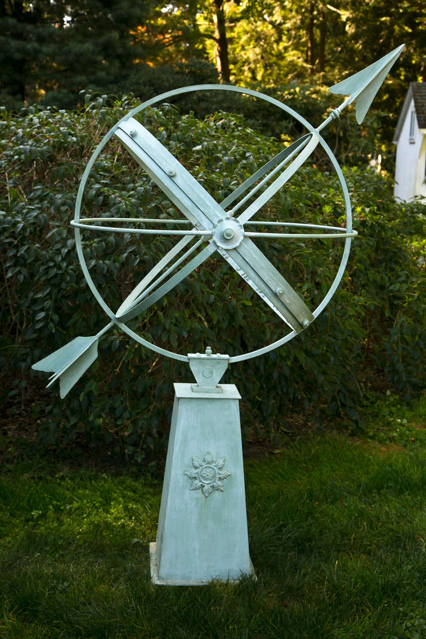 A steel armillary sphere on pedestal crafted by John Hardacre, a Connecticut-based artisan, the sphere with four celestial rings and an arrow, the tapered pedestal with rosette embellishments, light blue paint with white wash.