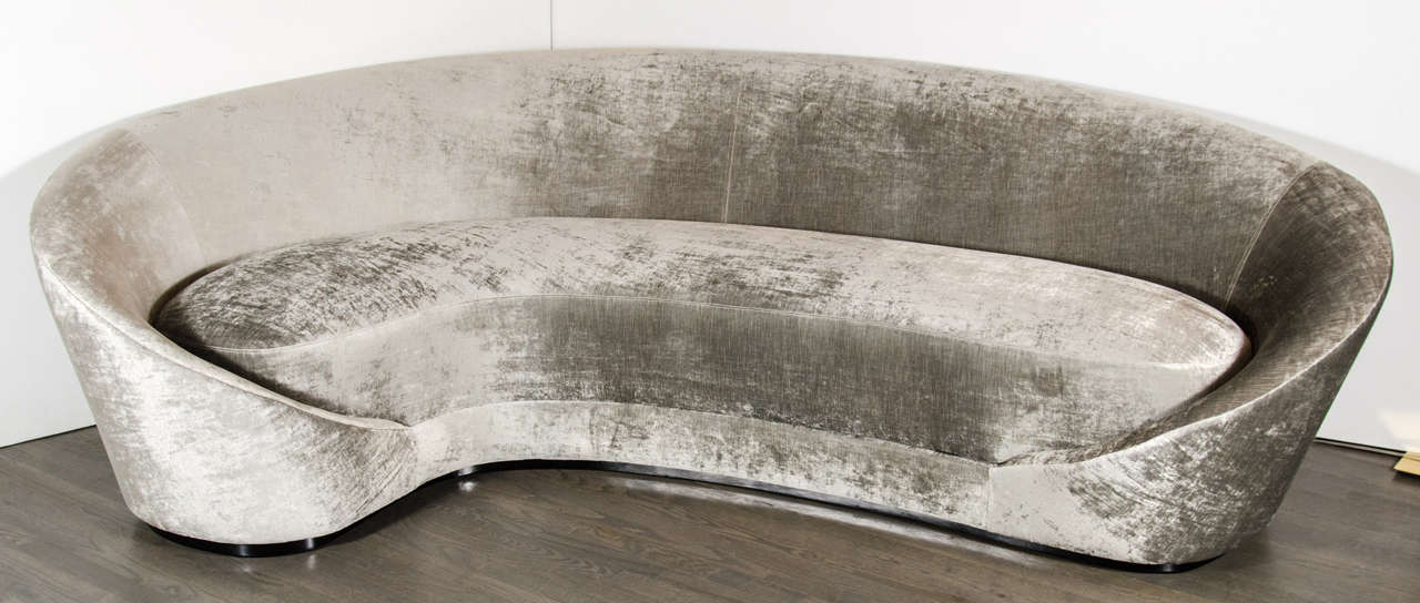 Luxurious 1940's curved sofa with a dramatic sweeping arm design sits atop an ebonized walnut platform and is upholstered in a luxe velvet of platinum and taupe tones.  This sofa will become the centerpiece to any room.Newly upholstered.