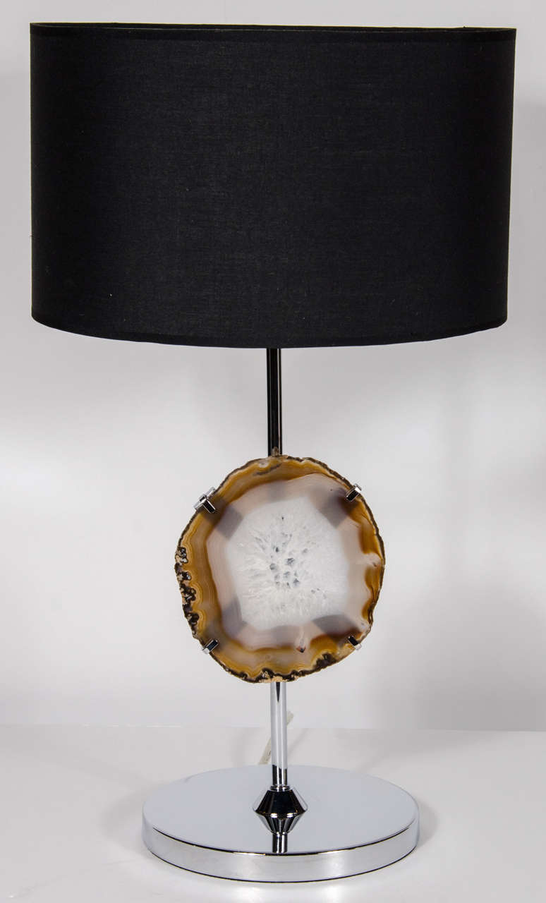 This dramatic chrome table lamp has a brilliant Luce Agate specimen in shades of Amber, Blue and Grey suspended by four prongs, just as natural stones are held in jewelry, on a simple chrome stem and base.  Topped with a custom black shade.  Newly
