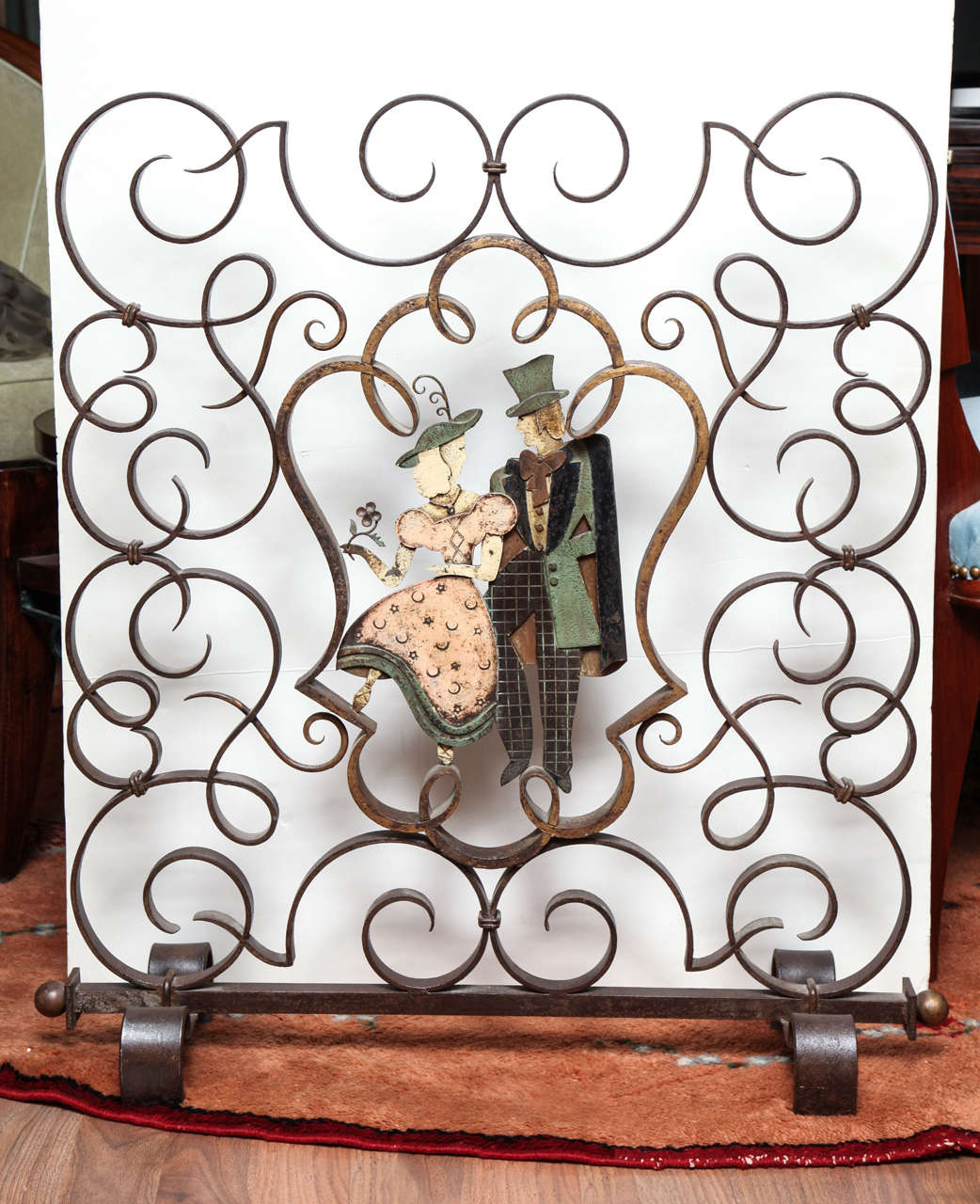 Art Deco figural fire screen in patinated and wrought iron with a motif of volutes and polychrome couple in the central medallion, French, 1930s. Measures: H 32.1 in (81.5 cm), L 29.5 in (75 cm).