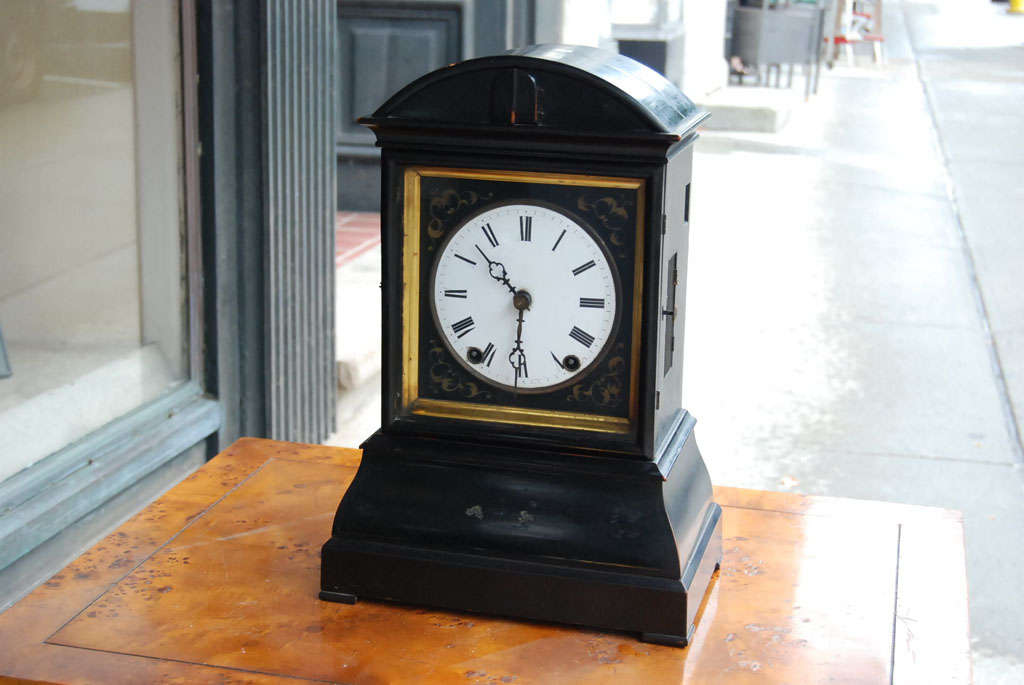 A most unusual and singular early Victorian clock with an ebonized wood case.  The enameled dial is set into a paint decorated surround, framed by a gilt wood molded frame behind a glass door.  The center of the domed top section has a pair of
