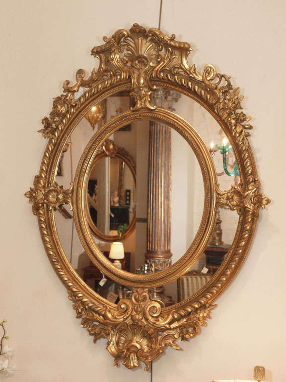 A fine pair of antique oval carved giltwood and gesso mirrors. Circa 1850-1870's. Pierced scrolled acanthus crest with floral sprays, divided mirror plate.