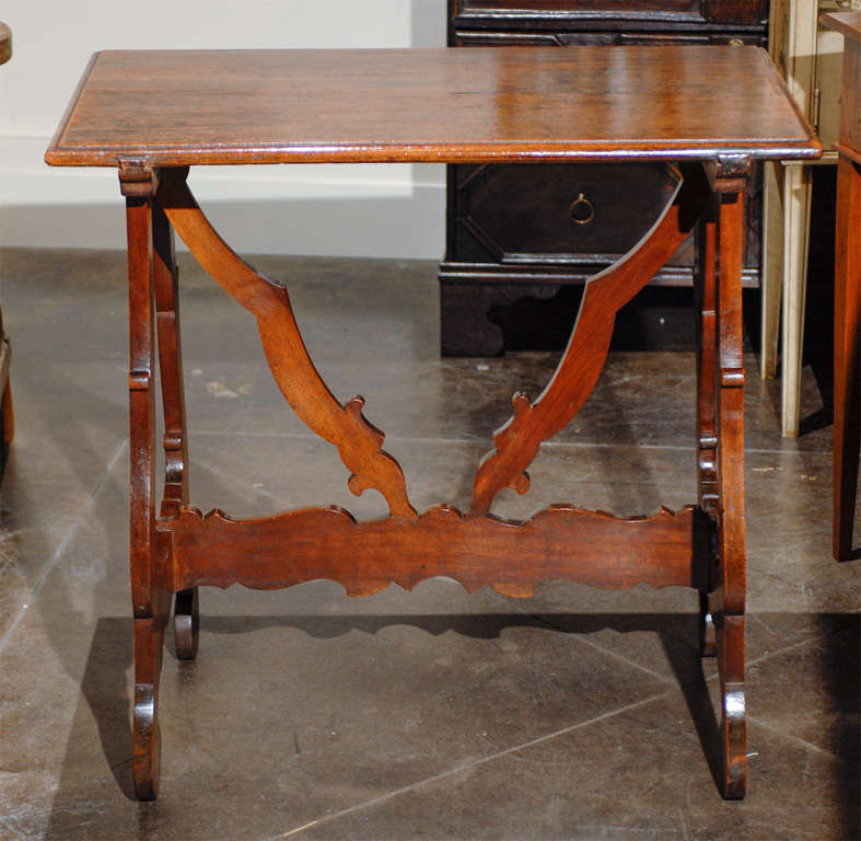 This Italian walnut side table from the late 18th century features a rectangular top with beveled edges over Baroque style lyre shaped legs with scrolled feet. The carved cross stretcher not only connects the legs, but also spreads vertically to