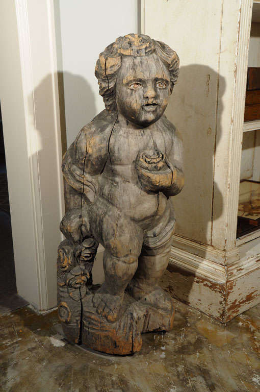 Carved, well worn wooden putto (chubby male angel, this one without wings).  He has lost one of his glass eyes so has been named 