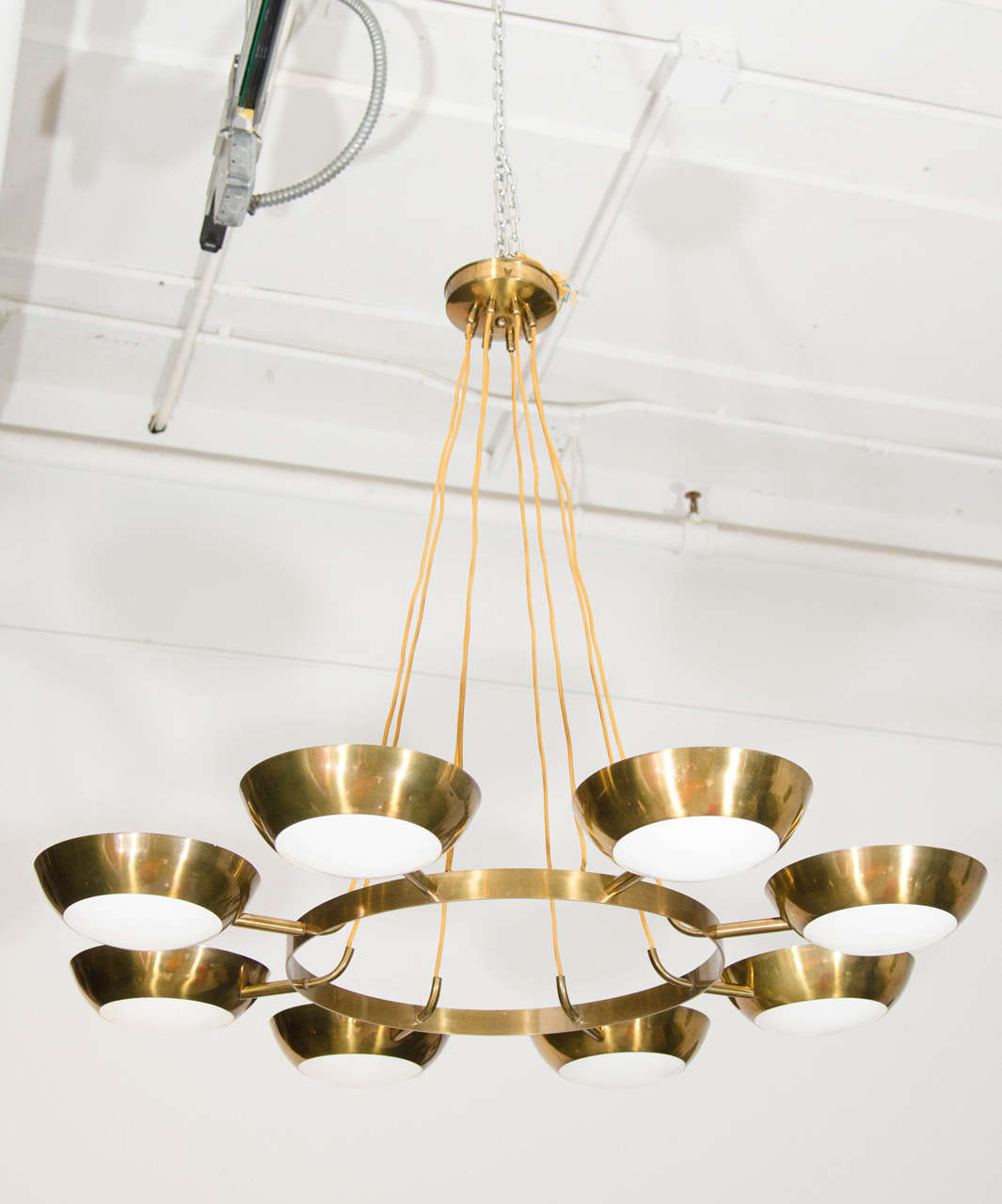 Eight brass cups are delicately illuminated with white glass lenses. A piece with presence but airy and modern.