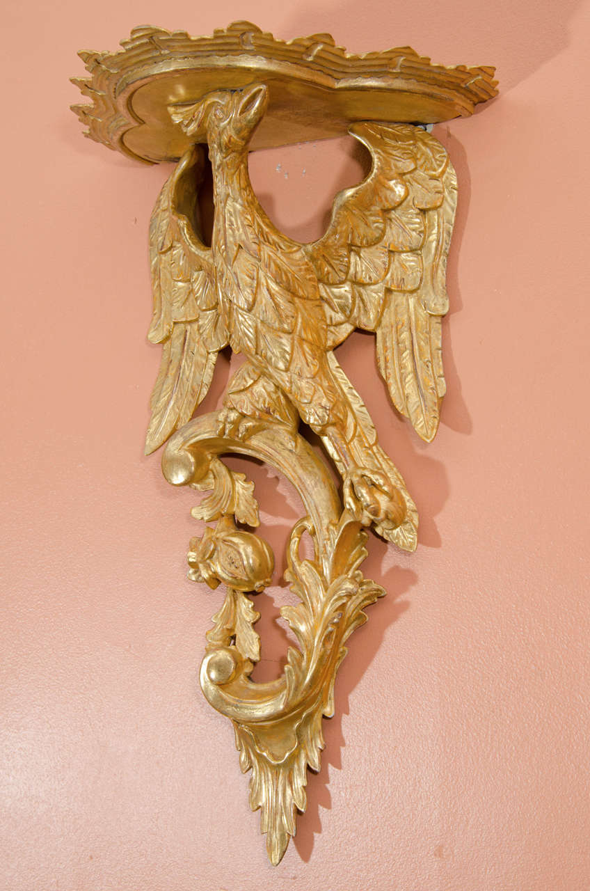 Pair of George III style Rococo giltwood brackets, the supports carved as phoenix birds atop C-scrolls with fruit pendants.